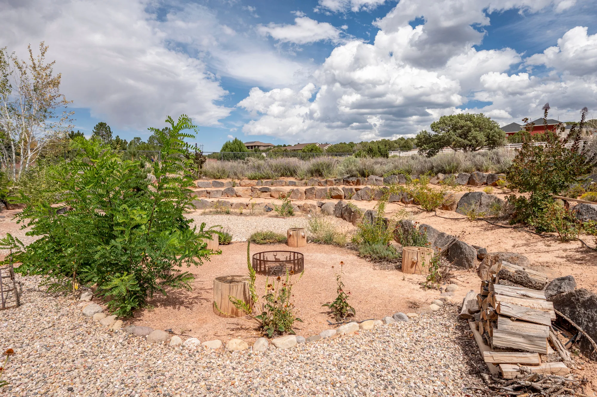 Terraced outdoor space with natural stone retaining walls, gravel pathways, a central fire pit, and mature landscaping