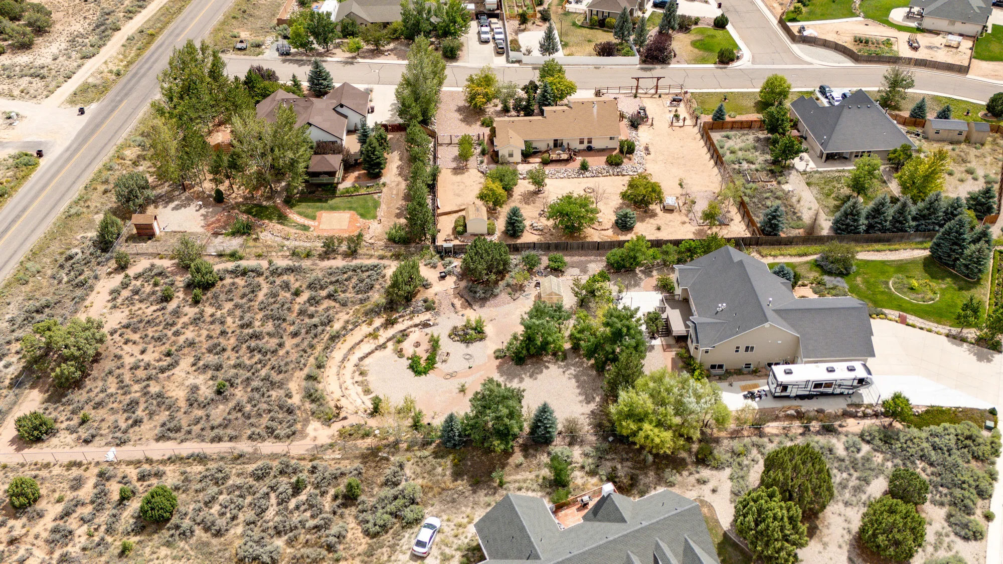Expansive property with a tan facade and dark gray roof, featuring mature trees and a substantial paved driveway