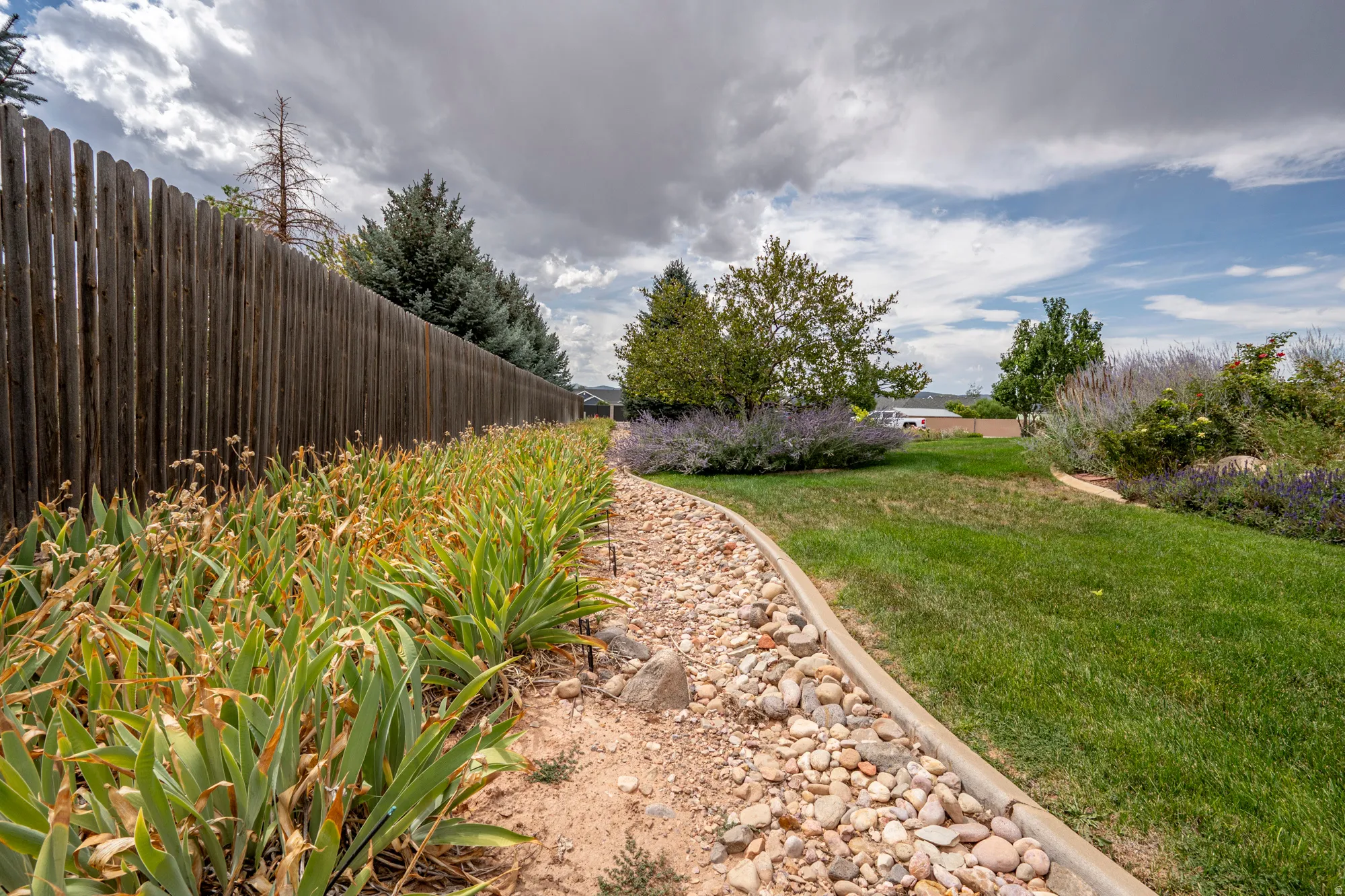 Expansive grassy area with a natural wood privacy fence, decorative rock landscaping, and mature perimeter trees