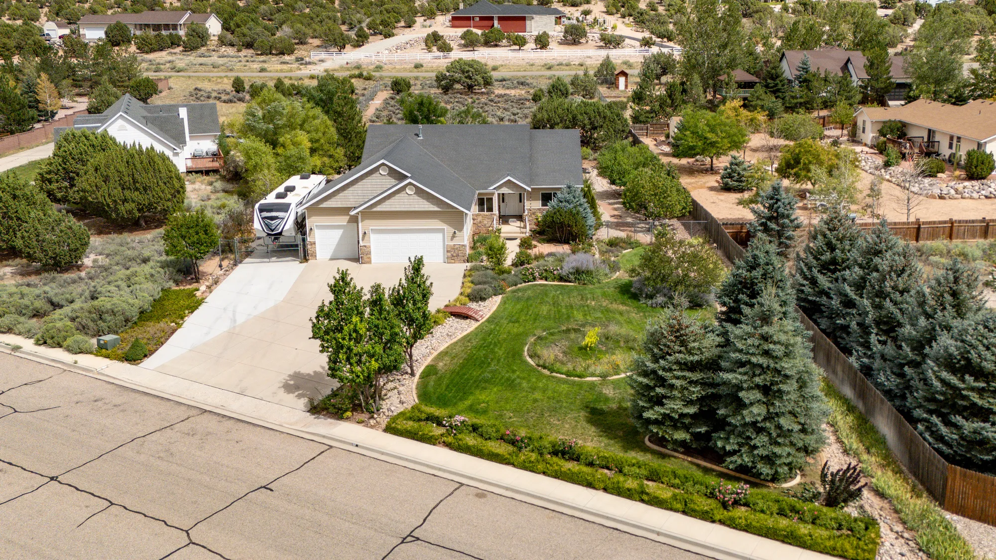 Two-car garage, concrete driveway, stone facade accents, front yard landscaping, and mature trees
