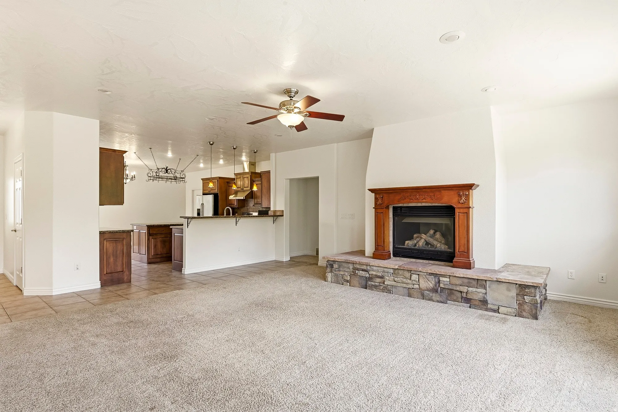Living area with a stone-clad fireplace and wood mantel, ceiling fan, and carpeted flooring