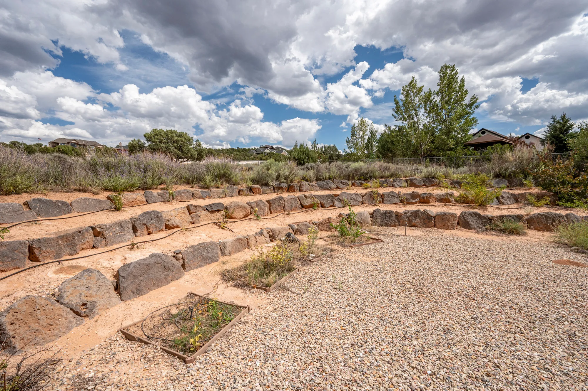 Terraced landscaping with natural stone retaining walls, integrated irrigation lines, and a gravel-covered ground area