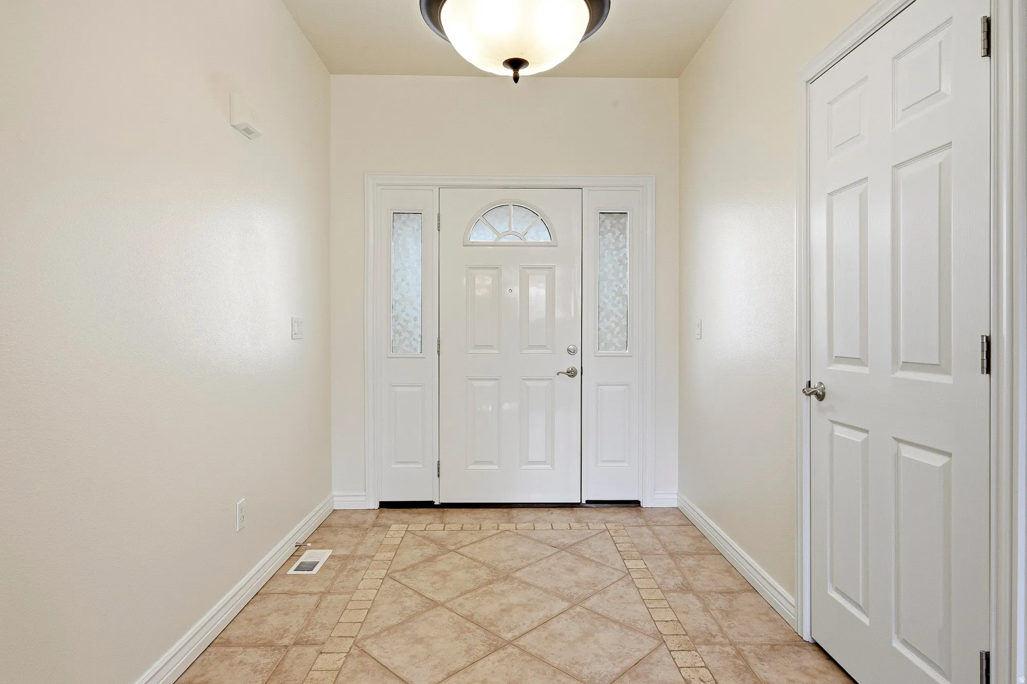 Entryway featuring a white paneled door, sidelight windows, arched transom window, and tile flooring with a decorative border