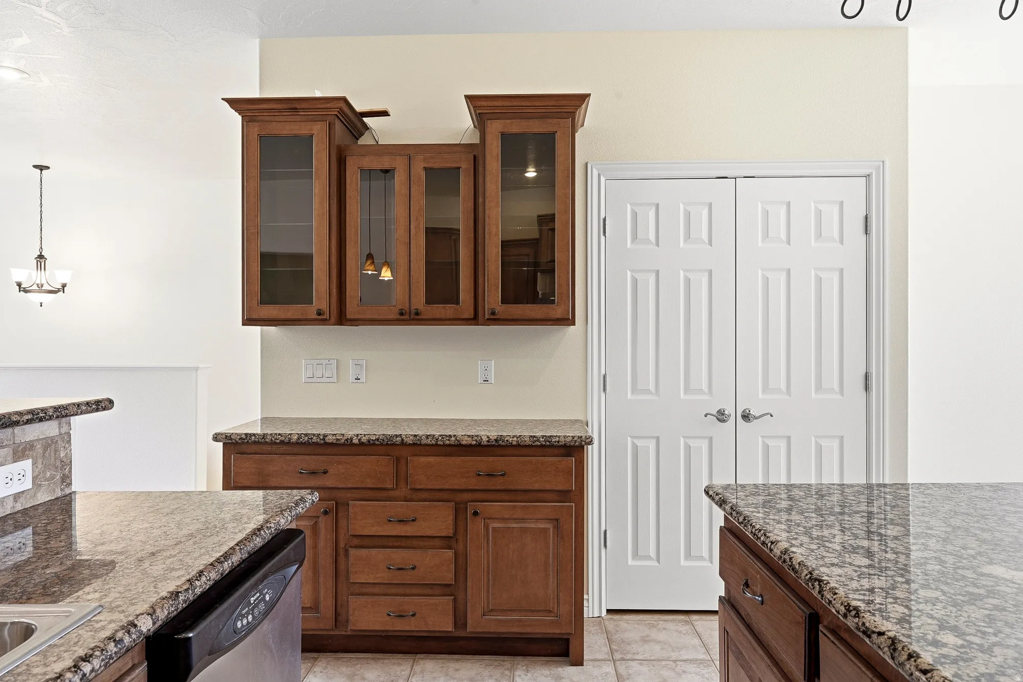 Wood-finish cabinetry with glass panel doors, granite-look countertops, and tile flooring