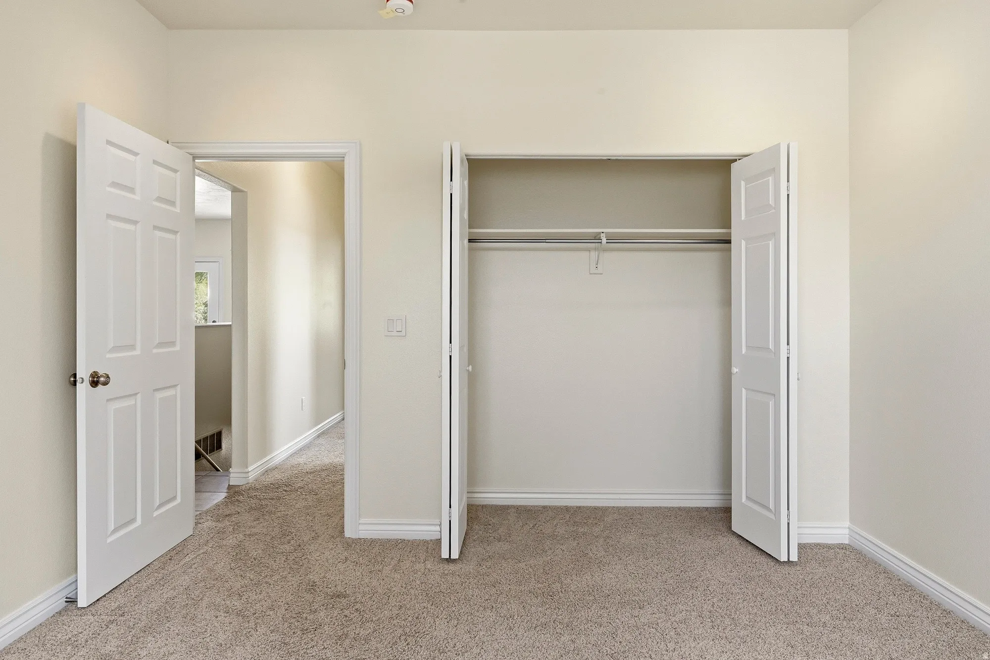Light beige wall paint, carpeted flooring, white trim, and a built-in closet with bi-fold doors