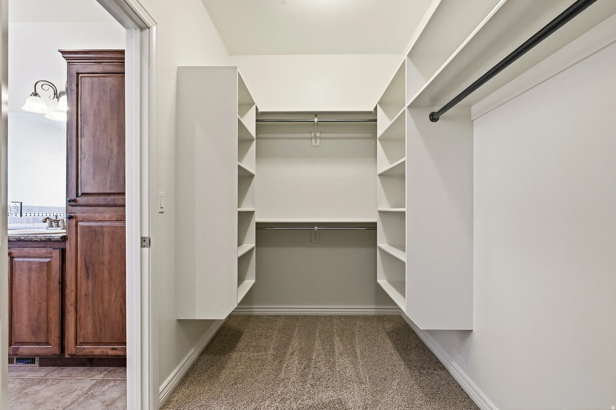 Walk-in closet featuring built-in shelving, multiple hanging rods, and neutral carpet