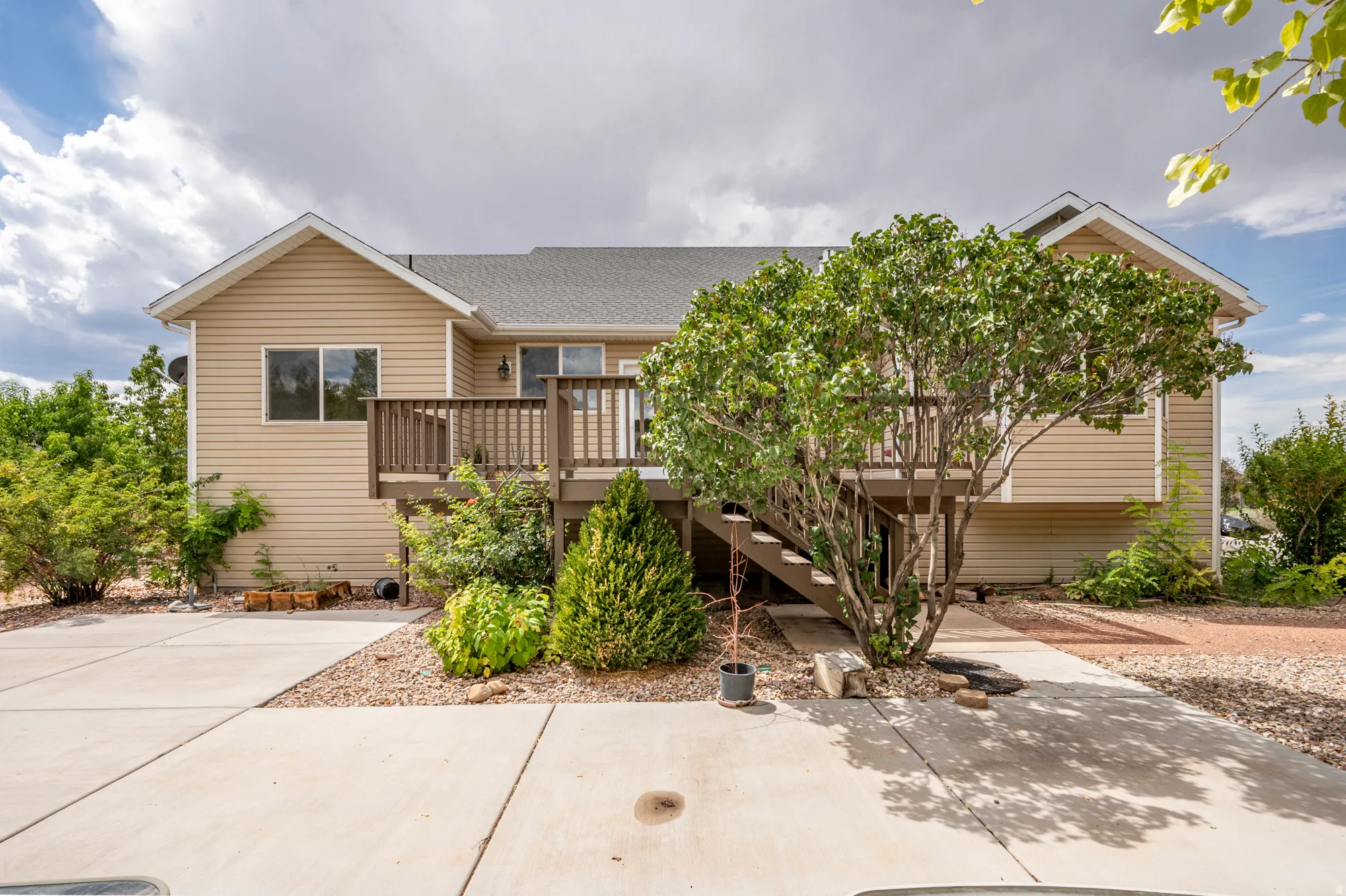 Rear exterior with a wood deck featuring stairs, light tan horizontal siding, and a gabled roofline