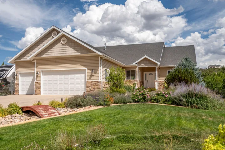 Exterior featuring horizontal siding, stone facade accents, a dark shingle roof, attached two-car garage, and a manicured lawn with mature landscaping