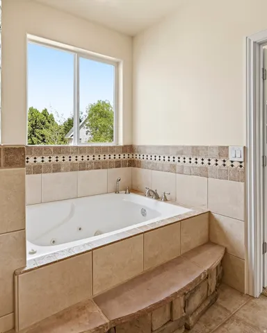 Built-in jetted tub with tile surround, decorative tile accent band, and an integrated stone-faced bench