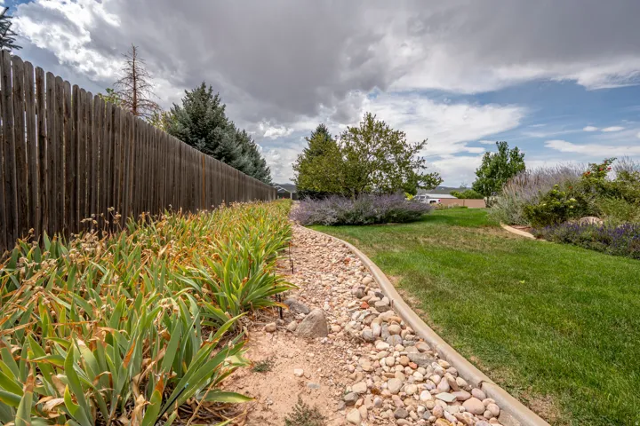 Expansive grassy area with a natural wood privacy fence, decorative rock landscaping, and mature perimeter trees