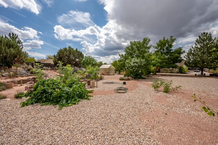 Expansive xeriscaped yard featuring gravel ground cover, mature trees, a dedicated garden area with raised beds, and a greenhouse structure