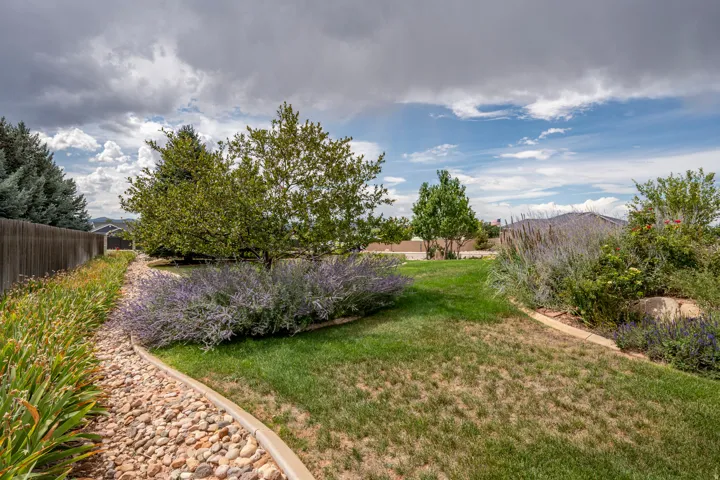 Landscaped backyard featuring a wooden fence, mature trees, and decorative plantings