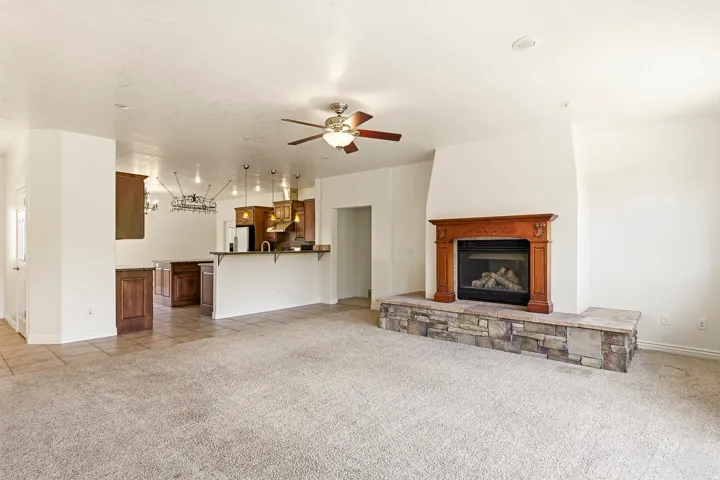 Living area with a stone-clad fireplace and wood mantel, ceiling fan, and carpeted flooring