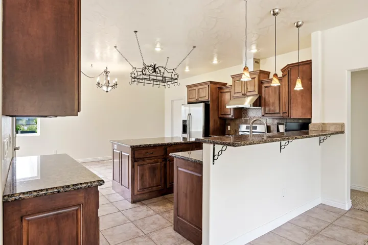 Kitchen featuring wood cabinetry, granite-style countertops, tile flooring, and stainless steel appliances