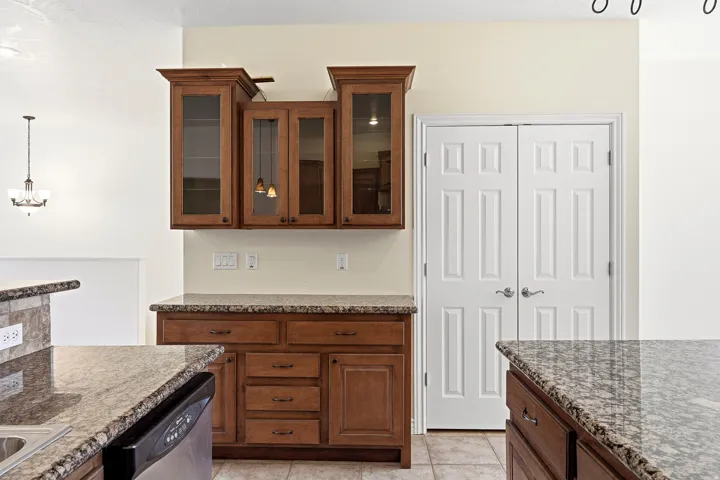 Wood-finish cabinetry with glass panel doors, granite-look countertops, and tile flooring