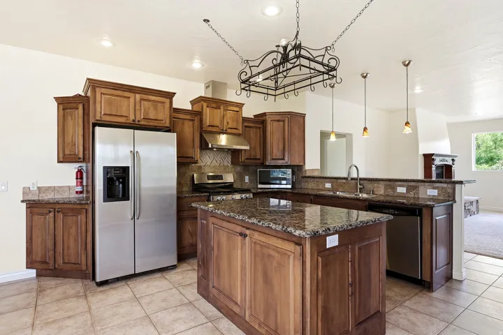 Kitchen featuring wood cabinetry, granite countertops, tile flooring, and stainless steel appliances