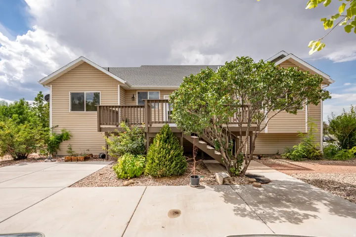 Rear exterior with a wood deck featuring stairs, light tan horizontal siding, and a gabled roofline