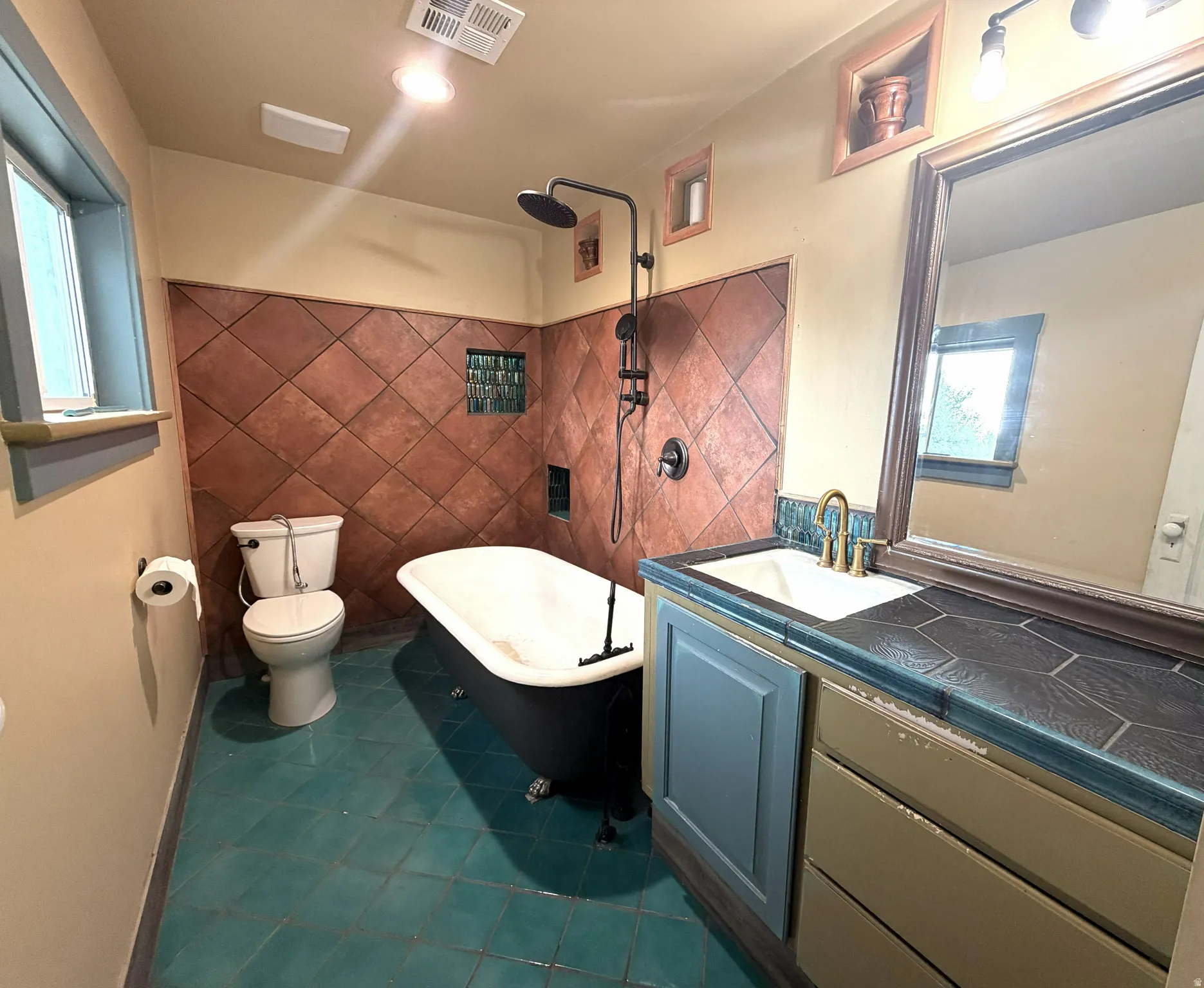 Clawfoot tub, floor-to-ceiling tiled shower surround, built-in shelving, vanity with integrated sink, and hexagon tile countertop