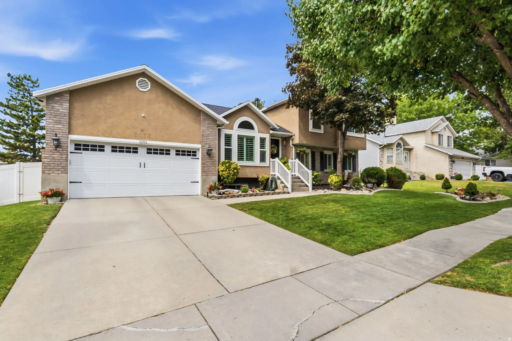 Stucco and stone exterior, attached two-car garage, concrete driveway, and front lawn with mature landscaping