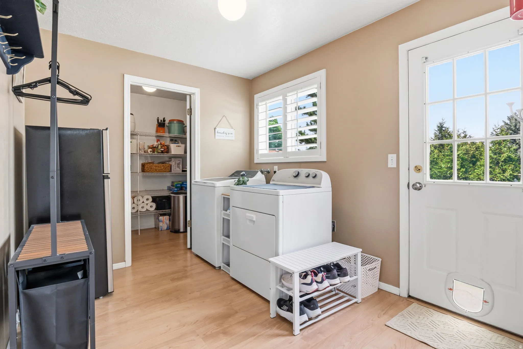 Laundry area featuring wood-finish flooring, white shuttered window, built-in pantry with wire shelving, and an exterior door with integrated pet access