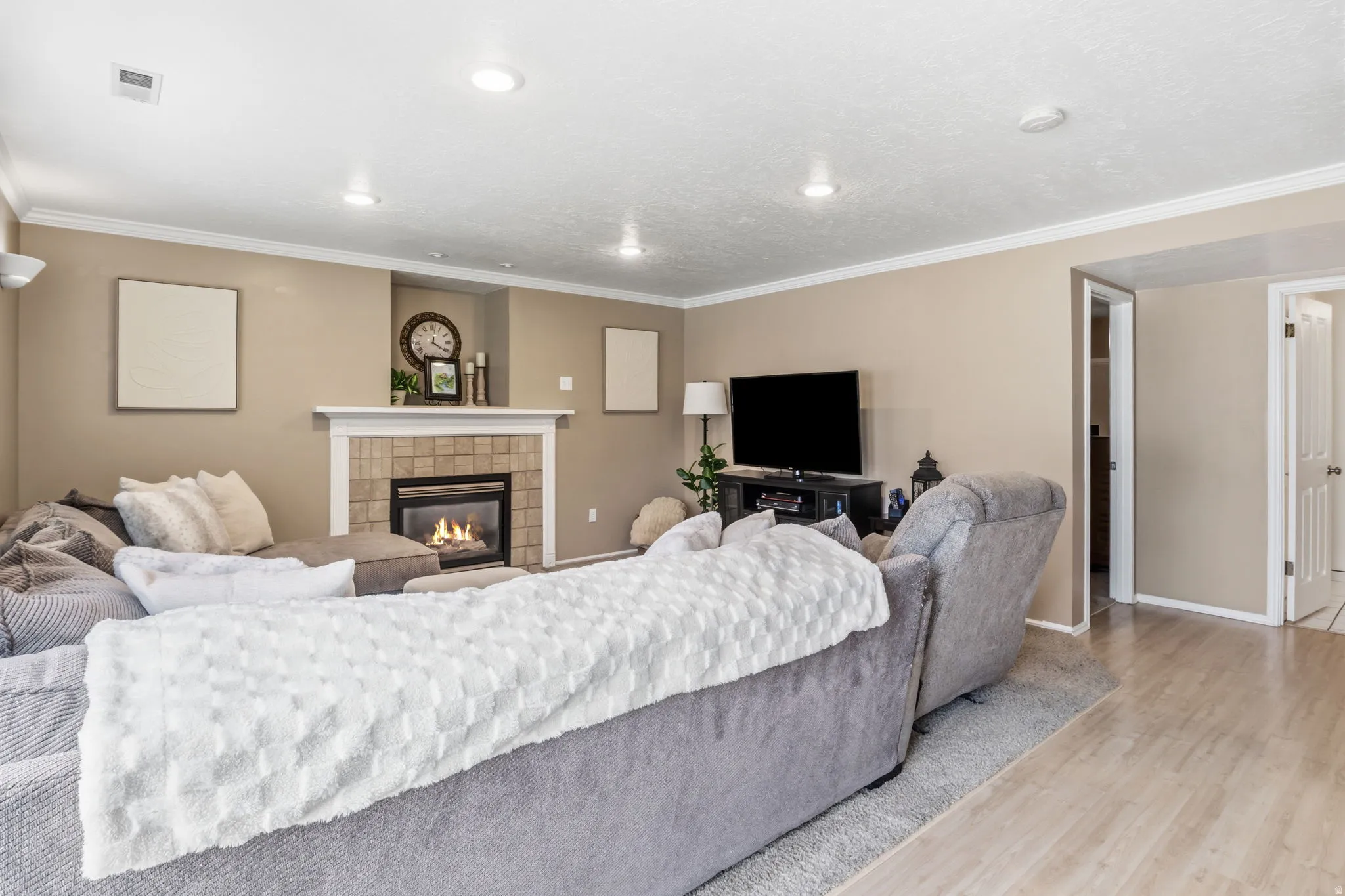 Tiled fireplace with a white mantel, recessed lighting, crown molding, and wood-finish flooring