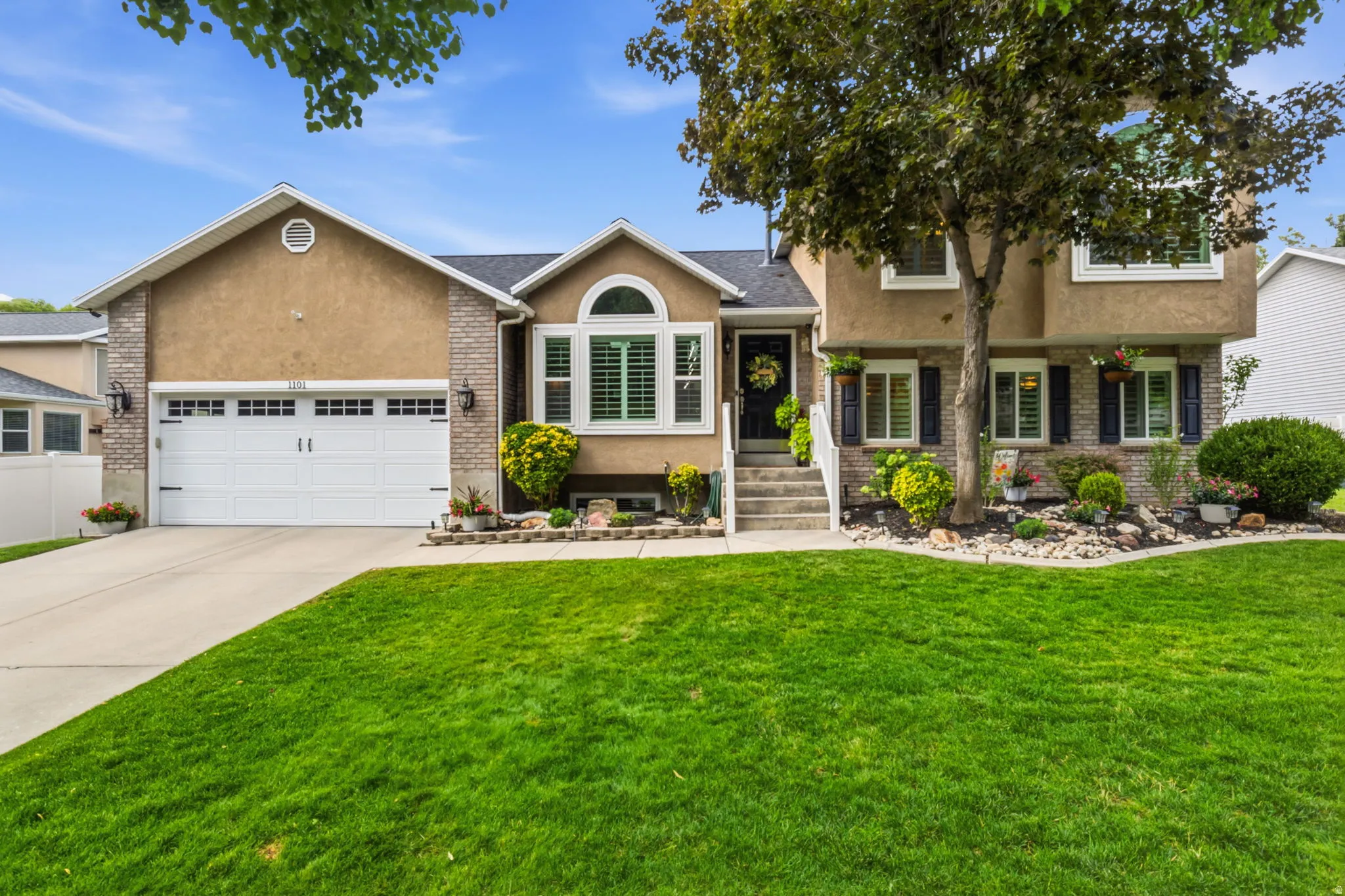 Stucco and brick facade with an arched window, white garage door, and established landscaping