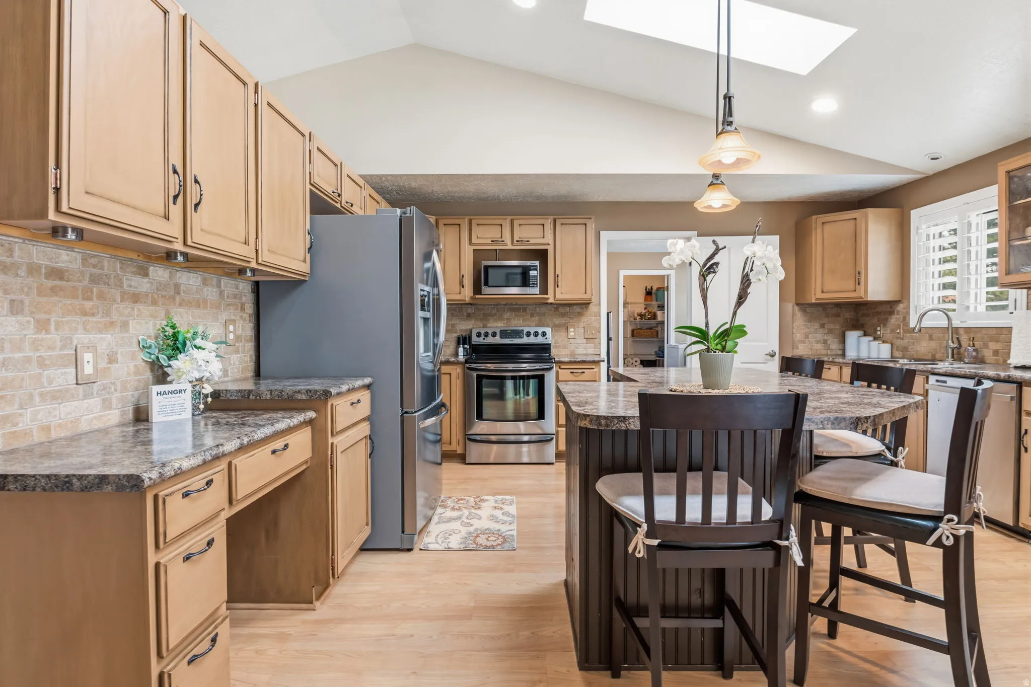 Vaulted ceiling with skylight, stainless steel appliances, wood-finish flooring, stone backsplash, and granite-look countertops