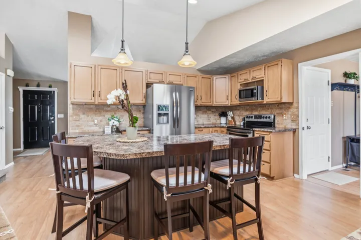 Kitchen featuring wood-finish flooring, a large central island with a multi-tone countertop, stainless steel appliances, and wood cabinetry