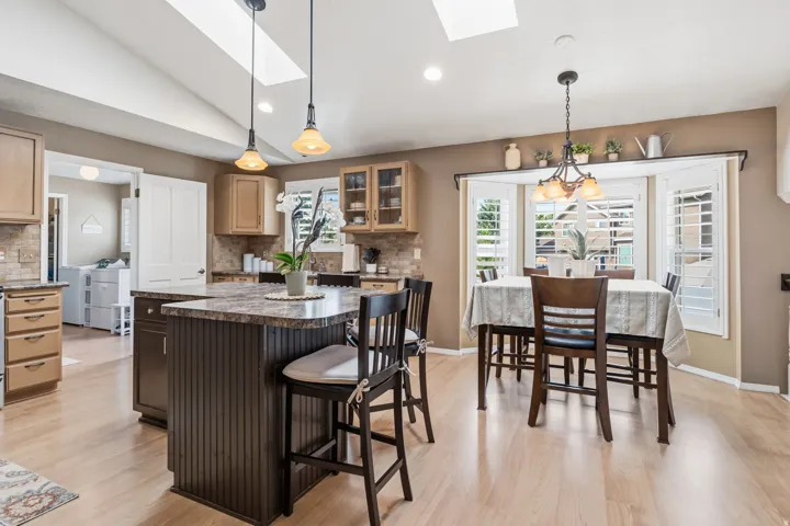 Vaulted ceiling with skylights, wood-finish flooring, kitchen island with built-in storage, bay window with plantation shutters, and pendant lighting