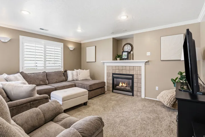 Recessed lighting, crown molding, wall sconces, window with plantation shutters, and a tiled fireplace with a white mantel
