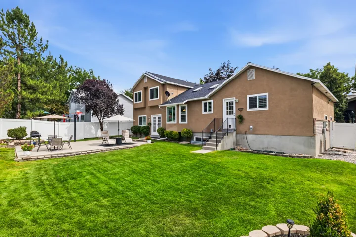 Expansive green lawn with a large patio area, white privacy fencing, and mature landscaping