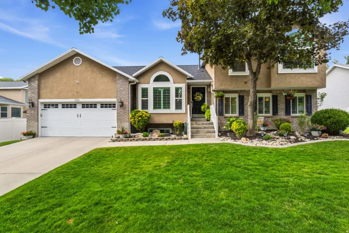 Stucco and brick facade with an arched window, white garage door, and established landscaping