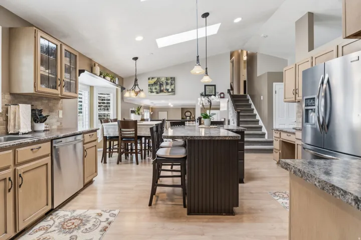 Kitchen featuring a center island, wood-finish flooring, stainless steel appliances, and vaulted ceilings with skylights