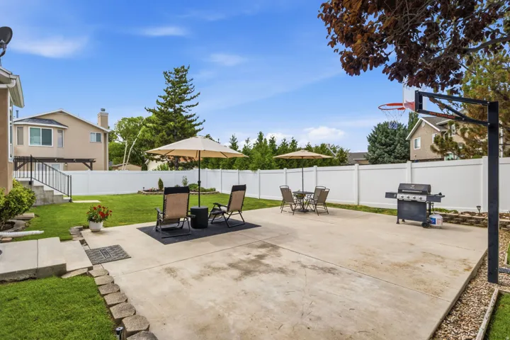 Expansive backyard featuring a large concrete patio, manicured lawn, and a full privacy fence