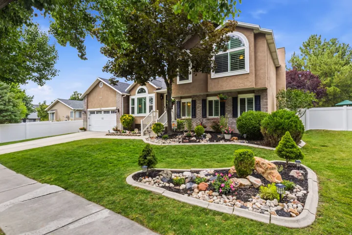 Landscaped front yard with mature trees, decorative rock beds, and a paved driveway