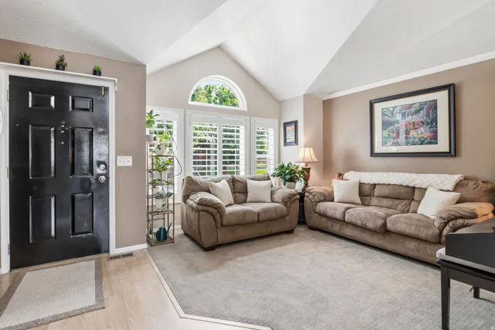 Vaulted ceiling, arched transom window, plantation shutters, light wood-finish flooring, and a paneled entry door