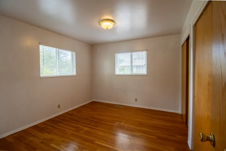 Hardwood flooring, two windows with blinds, flush mount ceiling light fixture, and a wood-finish closet door