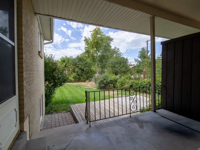 Covered concrete patio with decorative metal railing, leading to a wood-finish deck and a manicured lawn