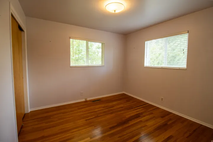 Hardwood flooring, two windows with blinds, flush mount ceiling light, and a built-in closet with a wood-finish door