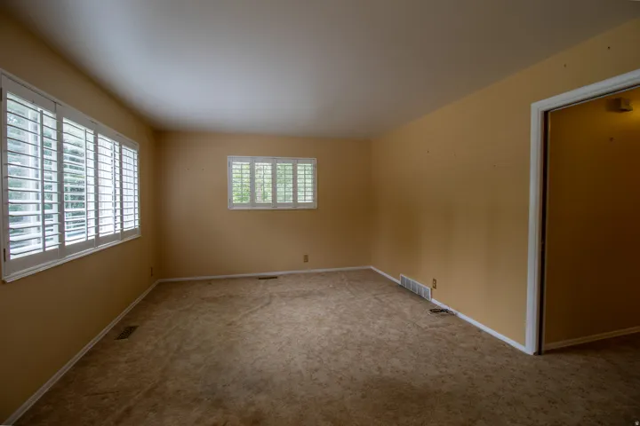 Two windows with plantation shutters, wall-to-wall carpeting, and neutral wall tones