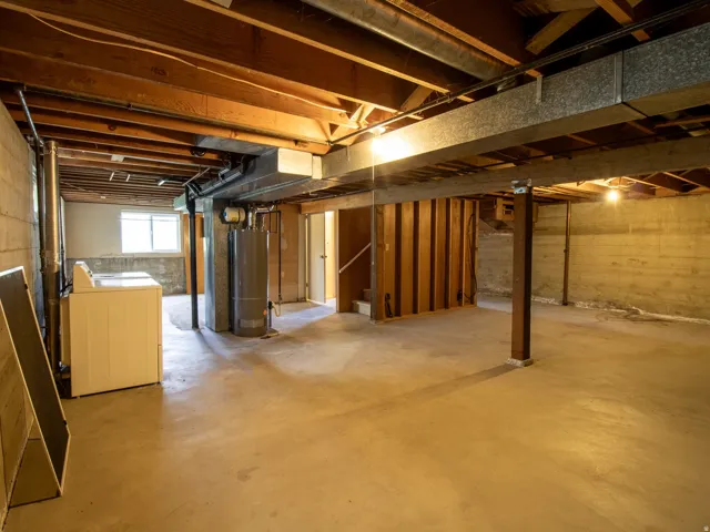 Unfinished basement featuring concrete flooring, exposed wood beams, concrete block walls, and a visible water heater
