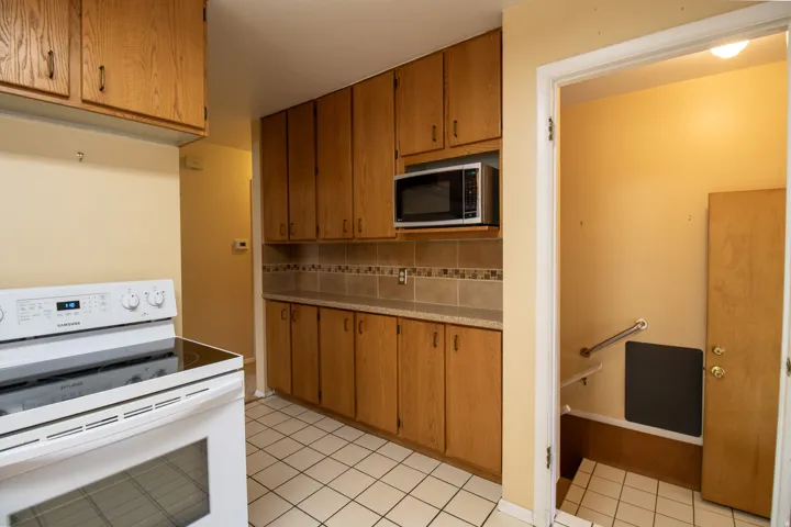 Kitchen featuring wood-finish cabinetry, tile backsplash, laminate countertops, and a white electric range with a black cooktop