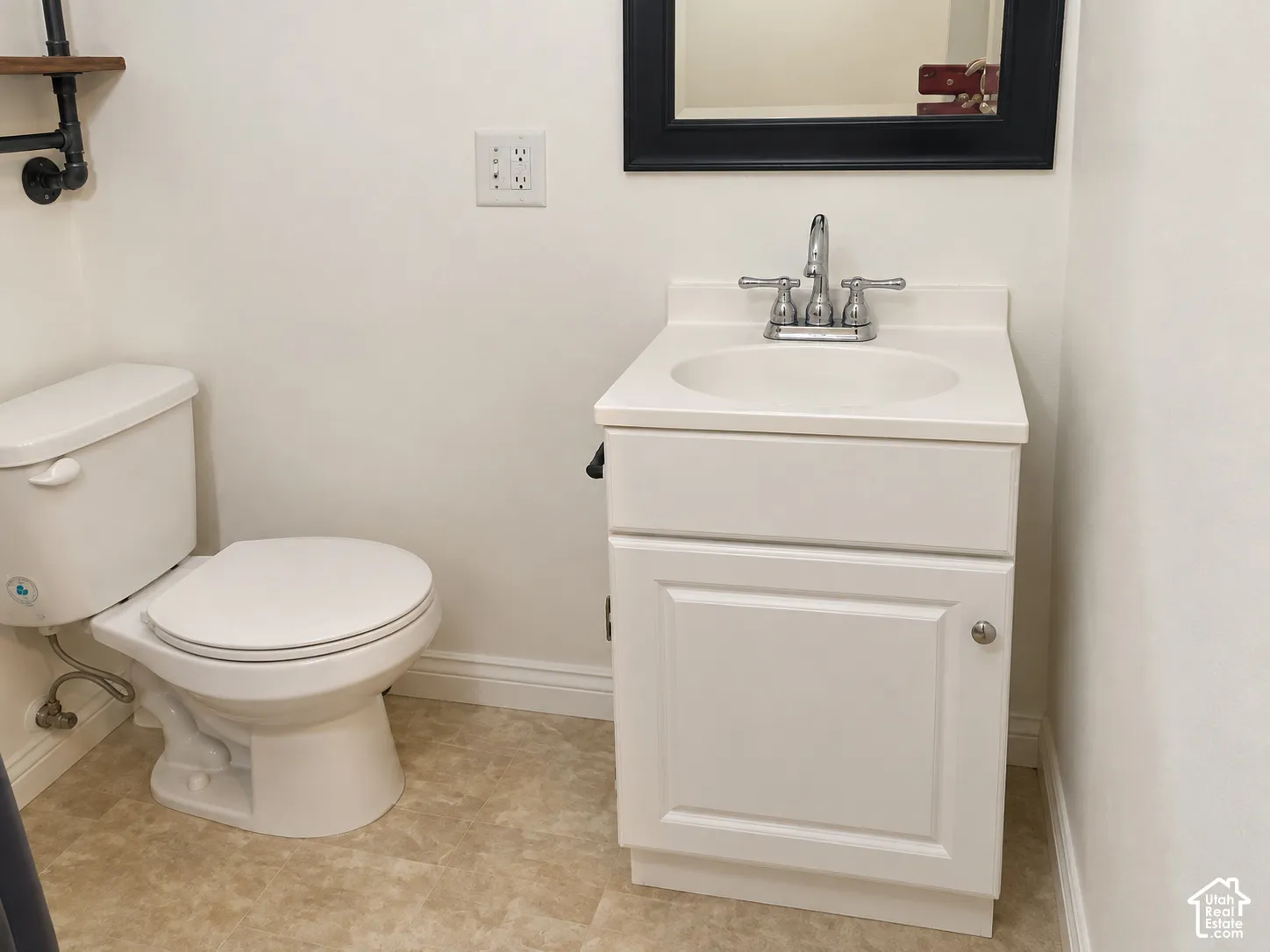 White vanity with a solid-surface countertop and integrated sink, chrome dual-handle faucet, elongated toilet, and neutral patterned flooring