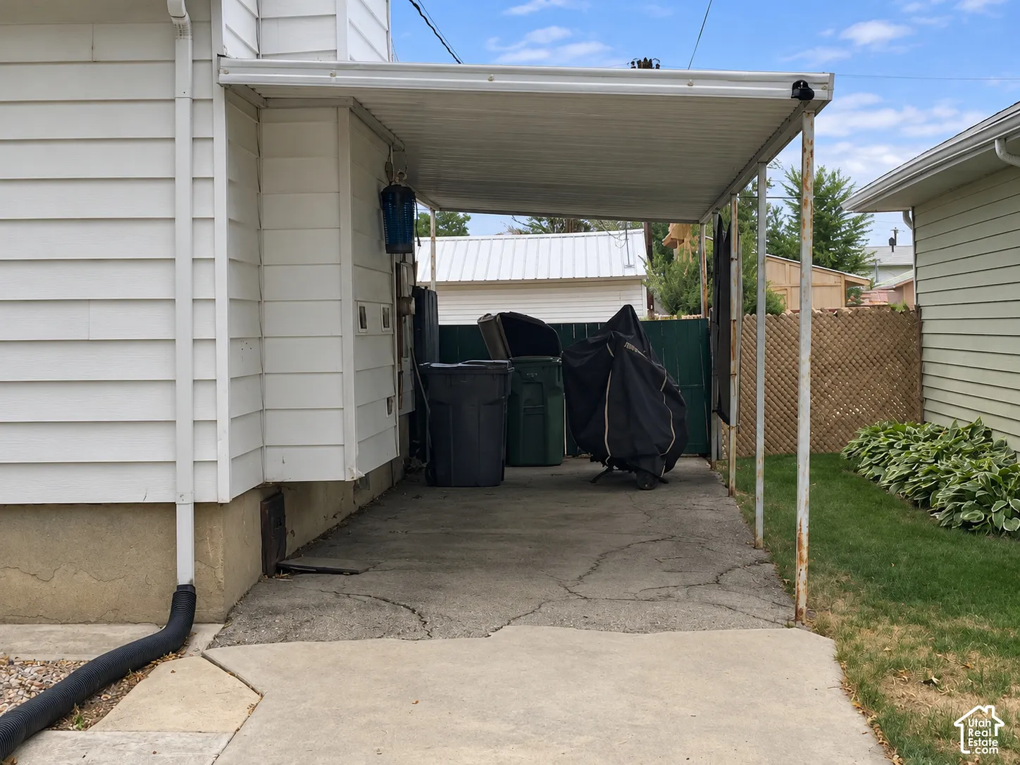 Covered carport featuring white horizontal siding, concrete flooring, and lattice fencing