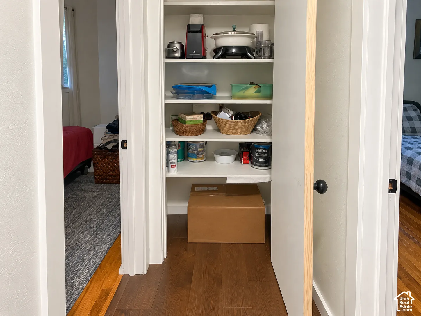 Built-in storage closet featuring four white fixed shelves and wood-finish flooring