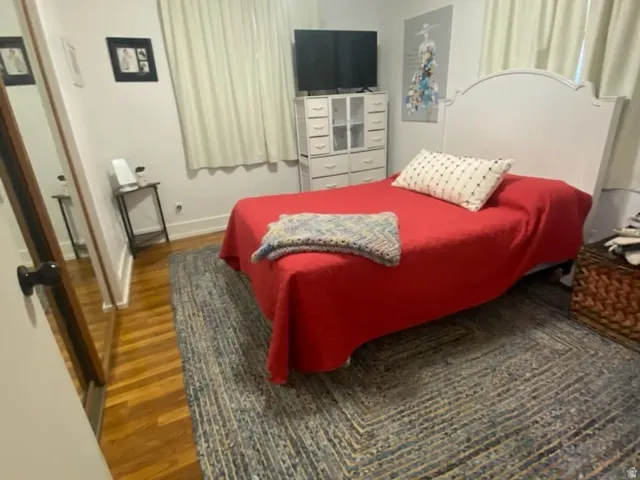 Hardwood flooring, flush-mount ceiling light, window with drapes, and a white headboard
