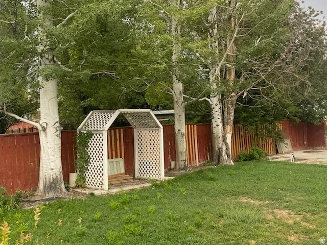 Lawn area featuring a white lattice arbor, mature trees, and a stained wood fence