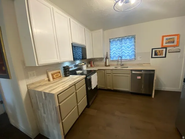 Kitchen featuring white upper cabinetry, light wood-finish countertops, a stainless steel dishwasher, a black range, and dark wood-finish flooring