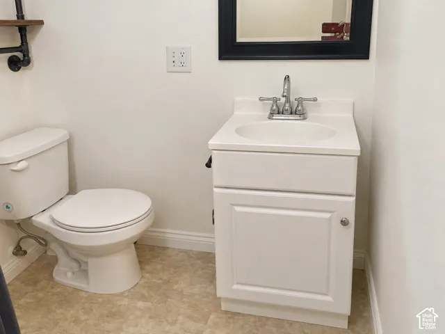 White vanity with a solid-surface countertop and integrated sink, chrome dual-handle faucet, elongated toilet, and neutral patterned flooring