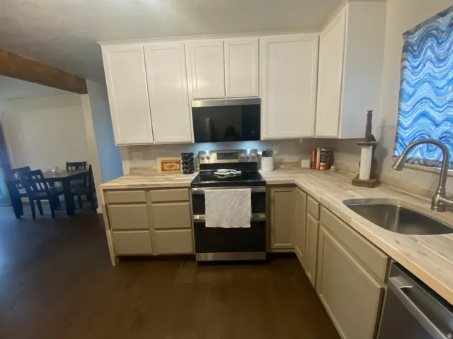 Kitchen featuring white upper cabinetry, light wood-finish countertops, stainless steel appliances, a stainless steel sink, and dark wood-finish flooring